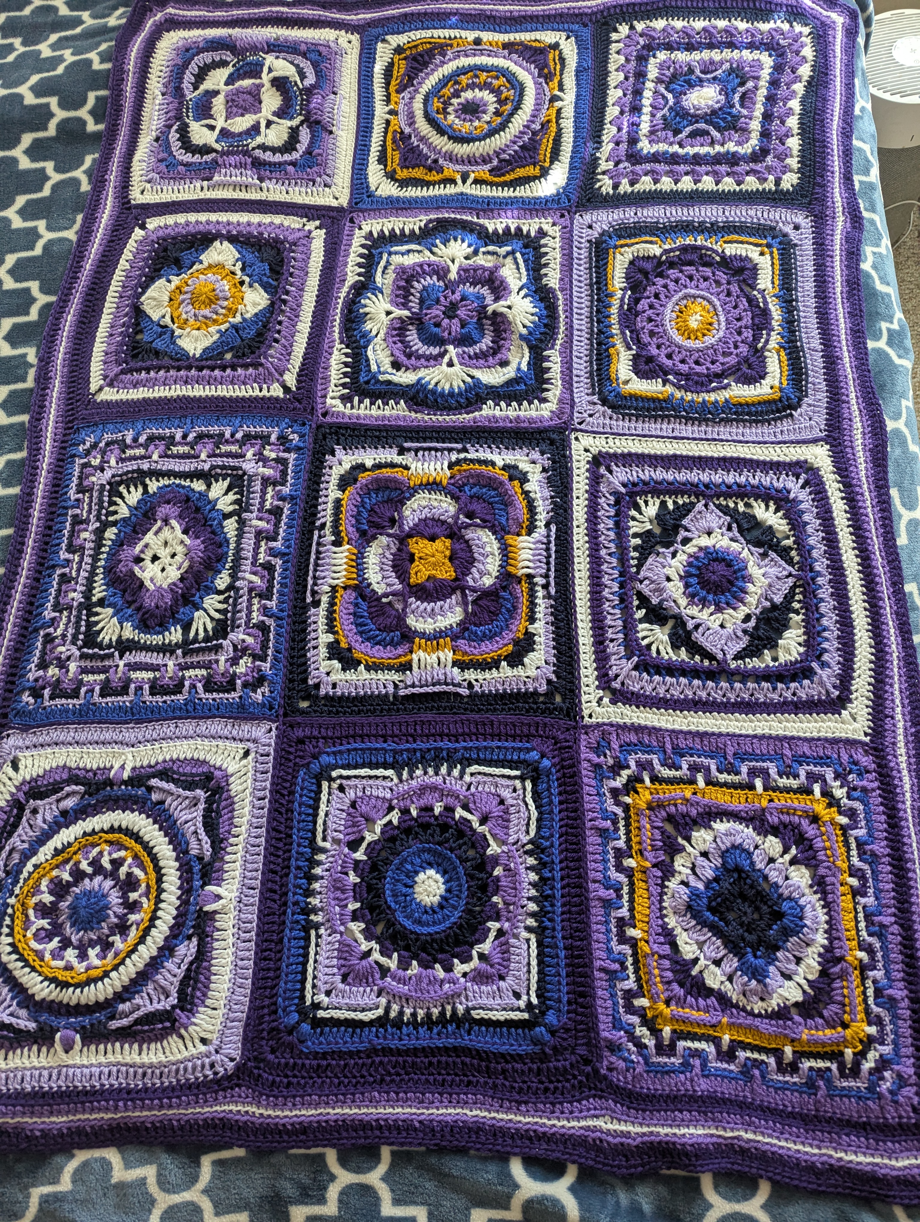 A purple, white, blue, and yellow crocheted blanket